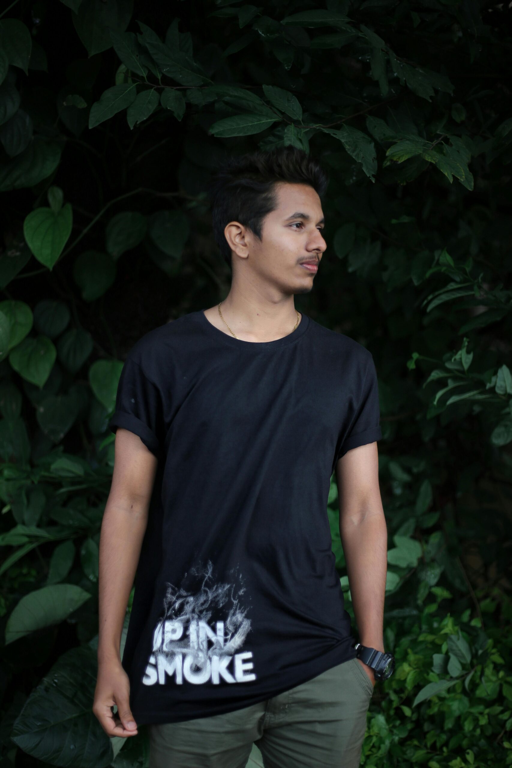 A young man poses casually outdoors against lush greenery in Bengaluru, India.